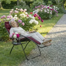 Červené záhradné relaxačné kreslo Lafuma FUTURA AirComfort v záhrade s kvitnúcimi kvetmi.